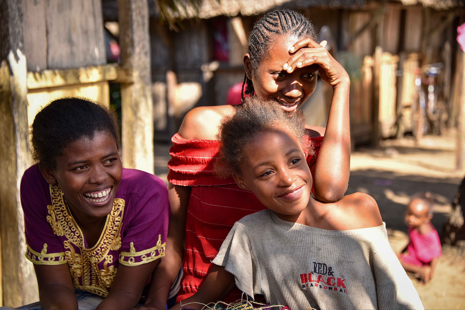 Three smiling young women and a girl relaxing together outside wooden homes in a village